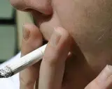 Nahaufnahme einer Hand, die eine brennende Zigarette hält. Der Rauch steigt auf und könnte Kopfschmerzen verursachen.