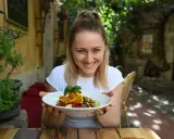 Uśmiechnięta kobieta prezentuje talerz pełen kolorowych warzyw, idealnych na dietę śródziemnomorską.