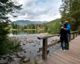 Coppia ammira il lago dei caprioli, con montagne sullo sfondo e una casa tra gli alberi.