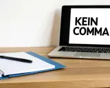 Ein Laptop zeigt "KEIN COMMA", während daneben ein Notizbuch mit Stift liegt.