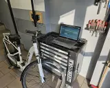 Profesjonalna naprawa rowerów elektrycznych w warsztacie. Biały rower elektryczny, laptop z oprogramowaniem diagnostycznym i zestaw narzędzi.