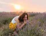 Frau kniet in einem Lavendelfeld und atmet den Duft ein. Die beruhigende lavendel wirkung psyche wird durch die warme Abendsonne unterstrichen.