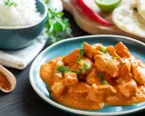 Sabroso pollo al curry cremoso servido en un plato azul, acompañado de arroz blanco, pan naan y especias.