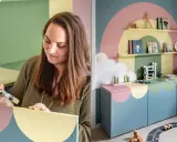 Kvinna målar hyllplan i pastellfärger för ett lekfullt barnrum. En regnbågsdesign pryder väggen och möblerna.