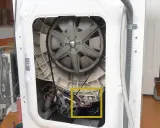 Innenleben einer Waschmaschine mit Riemenscheibe und Motor. Gelber Kasten markiert Bauteil, das bei einer Waschmaschine Unwucht verursachen könnte.