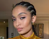 Primer plano de una mujer con trenzas, maquillaje de ojos con delineado y brillo, y labios brillantes.