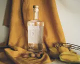 Butelka Cachaça Cãna, brazylijskiego alkoholu z trzciny cukrowej, otoczona owocami i suchymi liśćmi. Cachaca co to? To brazylijski skarb!