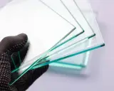Mano enguantada sostiene varias láminas de vidrio laminar de seguridad, mostrando su transparencia y bordes verdosos.