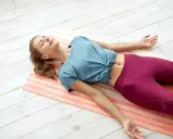Kobieta leży na macie, wykonując trening Jacobsona. Jej ciało jest rozluźnione, a oczy zamknięte.