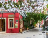 Ein rotes Gebäude mit weißen Tauben-Girlanden über einer Gasse in Chania, Kreta. Tische und Stühle laden zum Verweilen ein.