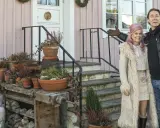 Melinda Jacobs och E-Type poserar glatt framför ett rosa hus med många krukor och en Buddha-staty.