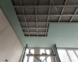 Instalación de falso techo de pladur para aislar techo ruido vecinos. Andamio y estructura metálica visibles.