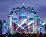 Castillo de luces y regalos en el parque navidad Torrejón. Artistas actúan en un escenario frente a la multitud.