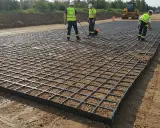 Trabajadores instalan una geomalla de refuerzo sobre grava para estabilizar el terreno en una obra.