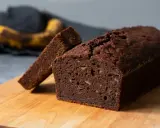 A slice of moist chocolate banana bread is propped against a whole loaf on a wooden cutting board.