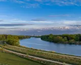 Wisła, jaka rzeka płynie przez Kraków, meandruje wśród zieleni. W oddali widać miejską panoramę.