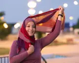 Lächelnde muslimische Frau mit buntem Hijab und Schal, der im Wind weht. Ein Bild, das die Vielfalt und Schönheit islamischer Kultur zeigt.