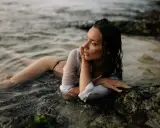 Modella in posa foto artistiche da fare al mare, sdraiata tra le rocce e l'acqua.