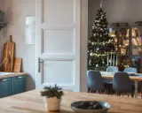 Julstämning i köket med en öppen dörr som avslöjar ett vackert julpyntat träd och en matsal. Perfekt jul inredning inspiration.