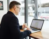 Hombre revisa en su laptop una cotización a tiempo parcial a efectos de jubilación, sentado en una cafetería.