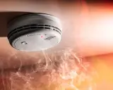 Brandvarnarens dag: en rökdetektor på taket med en röd lampa lyser, omgiven av dramatisk rök och ljus.