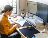 Mujer trabajando en un escritorio ordenado, con portátil, monitor curvo y plantas. Un ejemplo de como organizar tu escritorio para ser productivo.