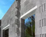 Ściana z bloczków betonowych, widoczny betonowy nadproże nad otworem okiennym. W tle zbrojenie i drzewa.