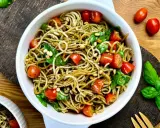 Leckerer Spaghetti-Salat zum Grillen mit Kirschtomaten, Pinienkernen und frischem Basilikum in einer weißen Schüssel.