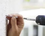 Mano insertando un tornillo en una pared texturizada, útil para saber si una pared es de pladur.