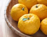 Kilka żółtych owoców yuzu w wiklinowym koszyku. Zastanawiasz się yuzu co to? To cytrus o intensywnym aromacie.