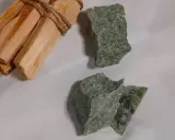 Surowe kawałki jadeitu w odcieniach zieleni, obok wiązki drewna palo santo.