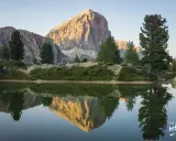 Riflesso perfetto di una montagna imponente nel lago di Limides, con alberi verdi e cielo azzurro.