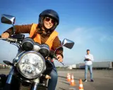 Uśmiechnięta kursantka na motorze, w kamizelce odblaskowej i kasku, uczy się jeździć. Zastanawiasz się, ile kosztują prawo jazdy na motor?