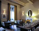 Salle à manger élégante avec tables dressées, prête à servir une spécialité de Provence. Lumière douce, rideaux ocre et gris, miroir orné.