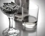 Kapsułki w kieliszku, obok szklanki z płynem. Czy niektóre leki zawierają alkohol etylowy?