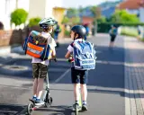 Deux enfants casqués, sacs à dos sur les épaules, se déplacent en trottinette. L'âge trottinette électrique est idéal pour ces jeunes écoliers.