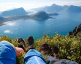 Fötter i vandringskängor vilar på en gräsbevuxen bergssluttning med en fantastisk utsikt över Lofoten. En perfekt dag för lofoten vandring.