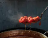 Gorące pomidory na łyżce cedzakowej, z których kapie sos.
