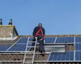 Un homme en harnais installe des panneaux solaires sur un toit. Un projet de panneau solaire installer soi-même en cours.