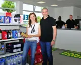 Ein Mann und eine Frau stehen vor Regalen mit Autoteilen und Ölflaschen.