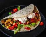 Ein köstliches Fajitas-Rezept: Tortilla gefüllt mit Hähnchen, Gemüse, Avocado und Sour Cream, garniert mit Tomaten.
