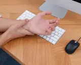 Main tenant une main sur son poignet, peut-être à cause d'une maladie du canal carpien, devant un clavier et une souris.