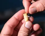 Dłonie wędkarza zakładają pellet na haczyk za pomocą gumki.