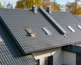 Szeroki dach pokryty ciemnoszarymi dachówkami ceramicznymi, z kilkoma oknami dachowymi i kominami. Różne rodzaje dachówek tworzą harmonijną całość.