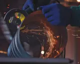 Manos enguantadas usan una radial para cortar un tubo, generando chispas. Un accidente con radial es un riesgo constante.