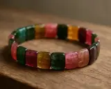 Bransoleta z wielobarwnych kamieni, w tym piękny turmalin różowy, ułożonych na drewnianym tle.