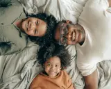 Un padre e i suoi due figli sorridono sdraiati sul letto, creando delle foto di famiglia originali e piene d'amore.