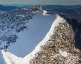 Två personer firar på toppen efter att ha lyckats bestiga Kebnekaise. Snö och sten dominerar landskapet.