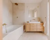 Elegancka, beżowa łazienka z drewnem. Wanna, umywalka i szafka z jasnego drewna tworzą przytulną atmosferę.