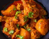 Un plat appétissant de poulet au curry, avec des morceaux de poulet tendres et des pommes de terre dans une sauce épicée, garni de coriandre fraîche.